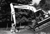 A digger working hard to hold back the hillside threatening the Lustleigh Village Hall